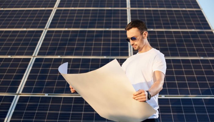 Businessman watching a plan on a background of solar panels. Young man with a clock in sunglasses, a white T-shirt and jeans familiarizes himself with an important document