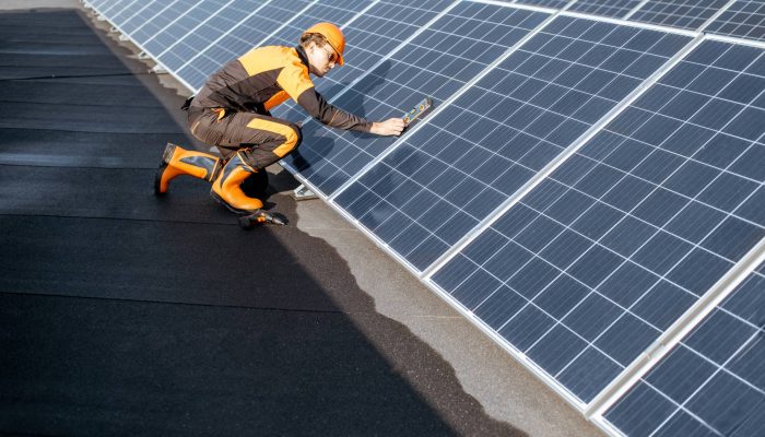Well-equipped worker in protective orange clothing installing solar panels, measuring the angle of inclination on a photovoltaic rooftop plant